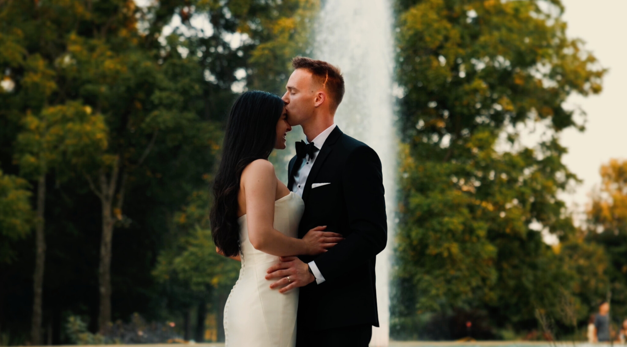 Lucas kissing Emma's forehead in front of a fountain